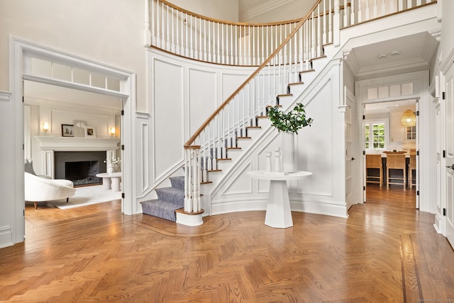 staircase with a decorative wall, a high ceiling, a fireplace, and crown molding