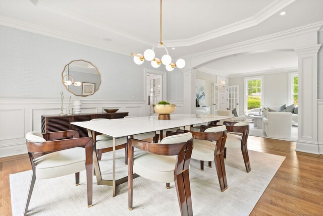 dining space featuring ornate columns, a decorative wall, ornamental molding, light wood-style flooring, and arched walkways