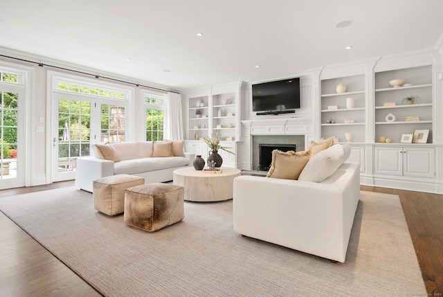 living area featuring wood finished floors, a fireplace, built in shelves, ornamental molding, and recessed lighting