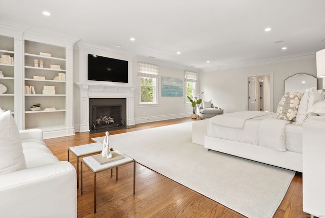 bedroom with crown molding, wood finished floors, a fireplace with flush hearth, and recessed lighting