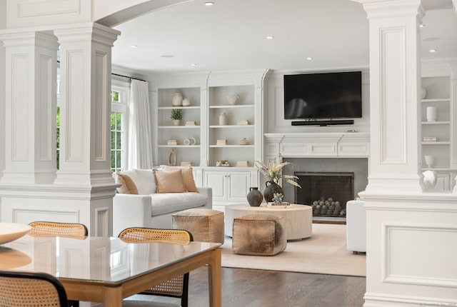 living area featuring ornate columns, arched walkways, wood finished floors, built in shelves, and recessed lighting