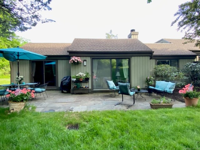 rear view of property with a yard, a patio area, roof with shingles, and a chimney