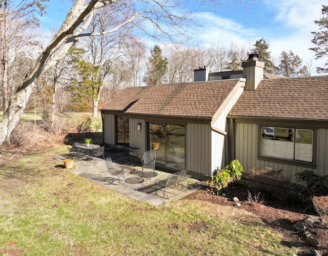 back of house with a patio area, board and batten siding, roof with shingles, and a chimney