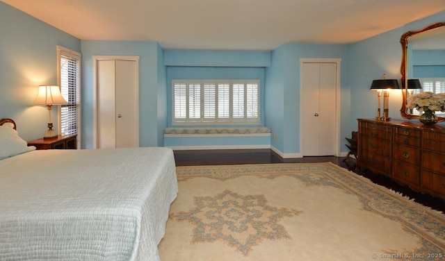 bedroom with baseboards, two closets, and wood finished floors
