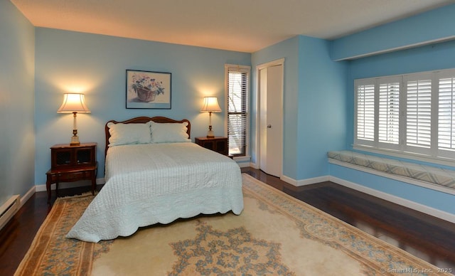 bedroom with baseboard heating, wood finished floors, baseboards, and a closet