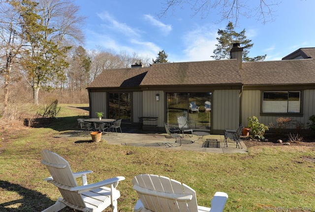 rear view of property featuring a patio area, a lawn, roof with shingles, and a chimney