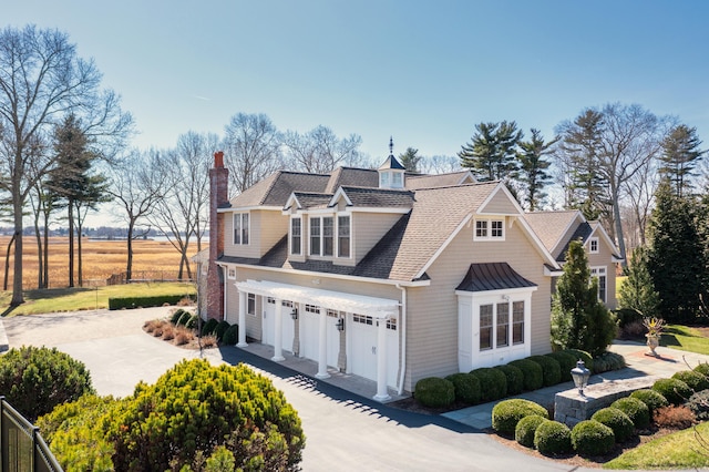 view of front of property featuring a chimney, driveway, a shingled roof, and a garage