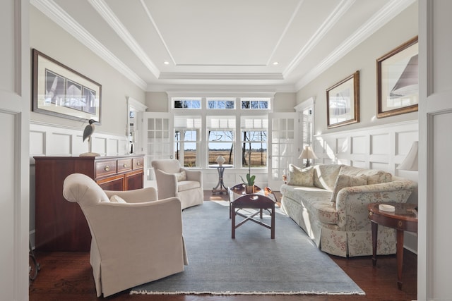 living room with crown molding, a wainscoted wall, a tray ceiling, and a decorative wall