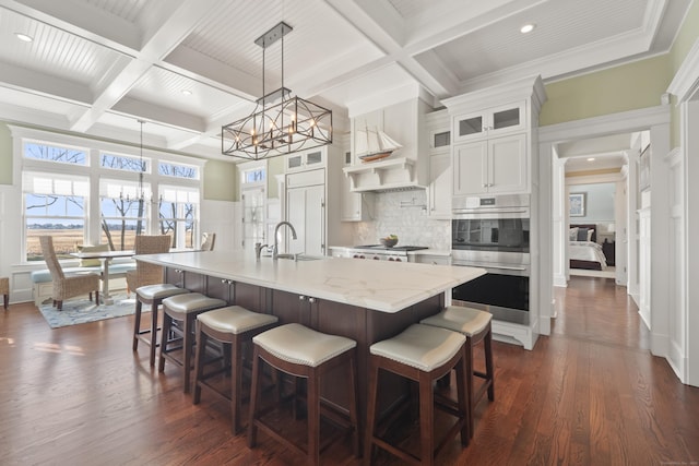 kitchen with beam ceiling, an island with sink, and coffered ceiling