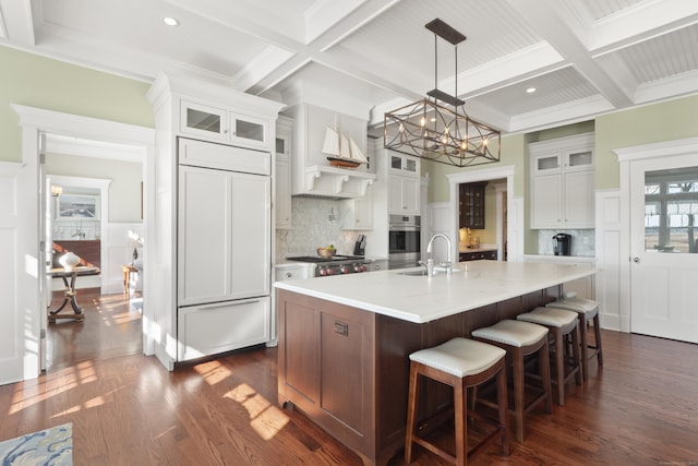 kitchen with tasteful backsplash, a chandelier, stainless steel oven, coffered ceiling, and dark wood-style flooring