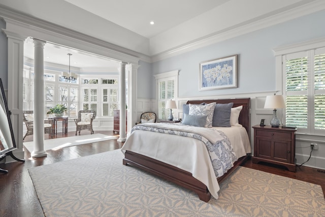 bedroom featuring crown molding, dark wood-type flooring, ornate columns, and a decorative wall