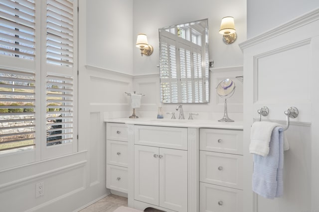 bathroom with a decorative wall, marble finish floor, vanity, and wainscoting