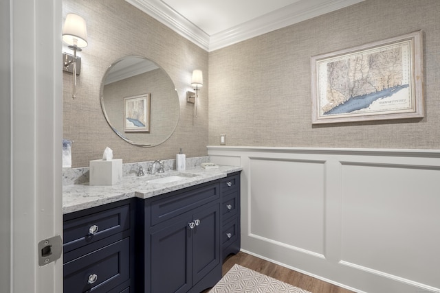 bathroom featuring a wainscoted wall, wood finished floors, vanity, ornamental molding, and a decorative wall