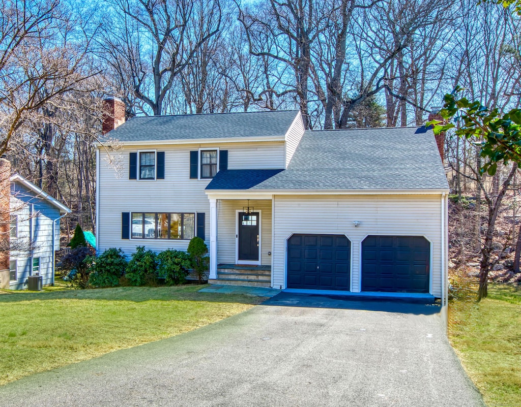 view of front of home with a shingled roof, a front lawn, aphalt driveway, cooling unit, and an attached garage