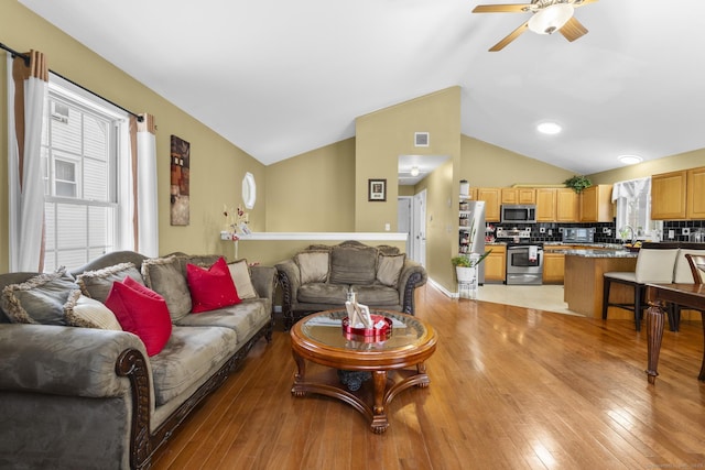 living area with plenty of natural light, a ceiling fan, light wood-style floors, and vaulted ceiling