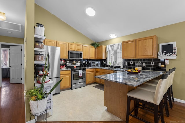 kitchen featuring decorative backsplash, a peninsula, vaulted ceiling, and stainless steel appliances