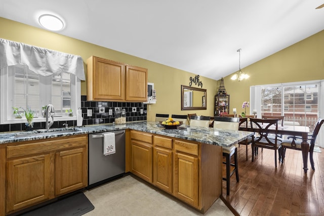 kitchen with dishwasher, vaulted ceiling, a peninsula, a kitchen breakfast bar, and a sink