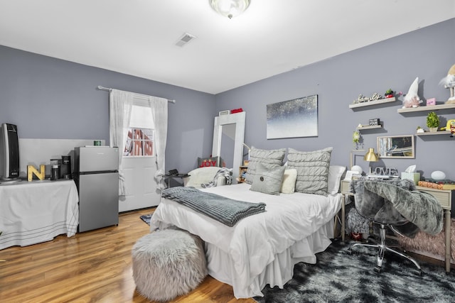 bedroom with visible vents, wood finished floors, and freestanding refrigerator