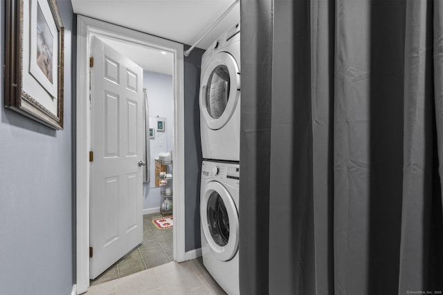 clothes washing area featuring laundry area, stacked washer / dryer, light tile patterned floors, and baseboards