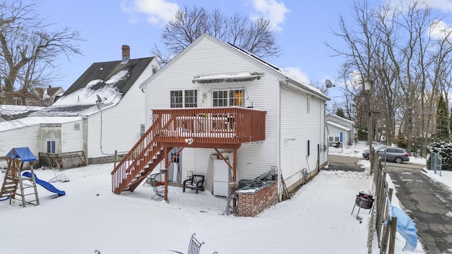 snow covered back of property with a wooden deck and stairway