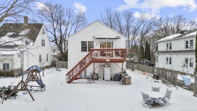 snow covered house with a wooden deck, stairs, and fence