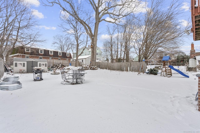 snowy yard with a fenced backyard, a storage shed, an outdoor structure, and a playground