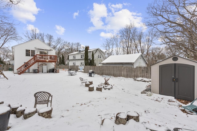 yard covered in snow with a storage unit, fence, stairway, an outdoor structure, and a wooden deck