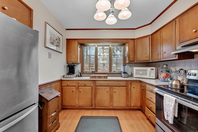 kitchen featuring light countertops, light wood-type flooring, brown cabinetry, stainless steel appliances, and decorative backsplash