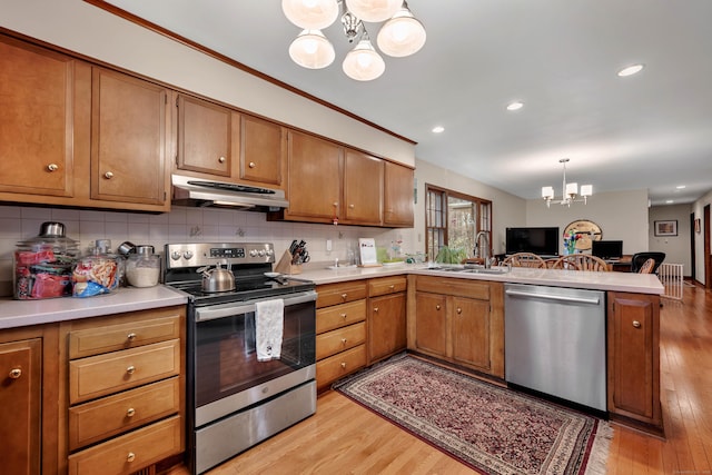 kitchen featuring an inviting chandelier, under cabinet range hood, a sink, a peninsula, and appliances with stainless steel finishes