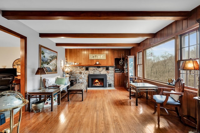 living room featuring a stone fireplace, beamed ceiling, wooden walls, and light wood-style flooring
