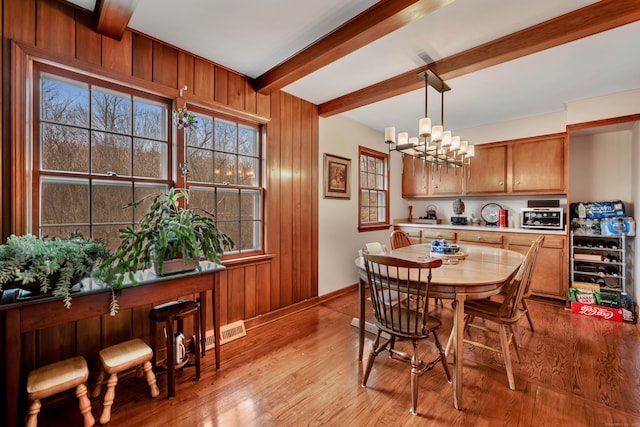 dining area featuring a chandelier, light wood finished floors, wood walls, visible vents, and beamed ceiling
