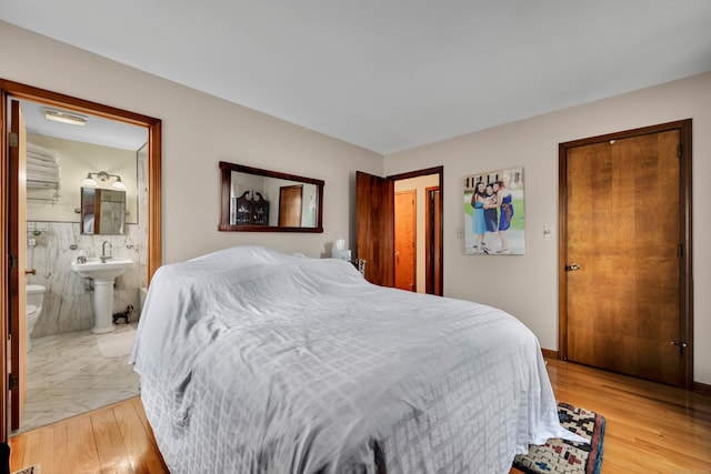 bedroom featuring a sink, ensuite bathroom, tile walls, and light wood-type flooring