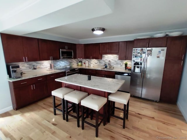 kitchen with a sink, appliances with stainless steel finishes, a kitchen bar, light wood-style flooring, and decorative backsplash