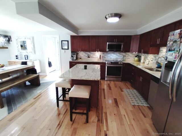 kitchen with light stone countertops, tasteful backsplash, light wood-type flooring, a center island, and appliances with stainless steel finishes