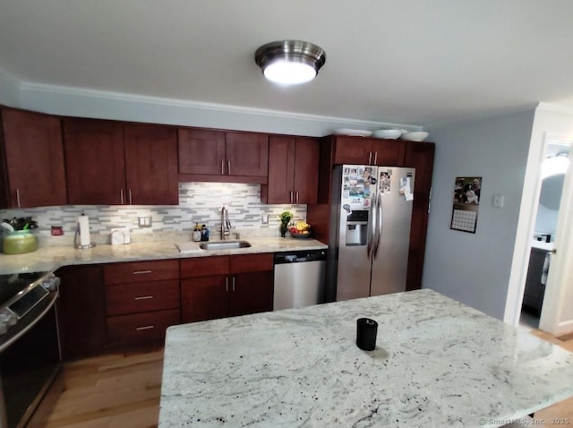 kitchen with tasteful backsplash, light wood-type flooring, appliances with stainless steel finishes, light stone counters, and a sink