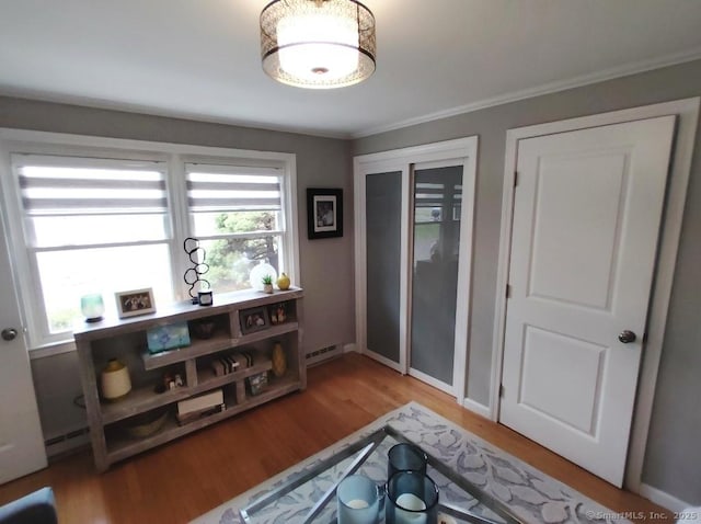 interior space with ornamental molding, a baseboard radiator, wood finished floors, and baseboards
