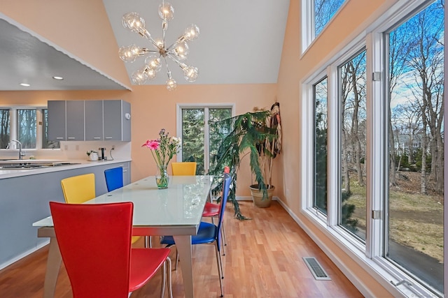 dining space with high vaulted ceiling, a chandelier, baseboards, and light wood-type flooring