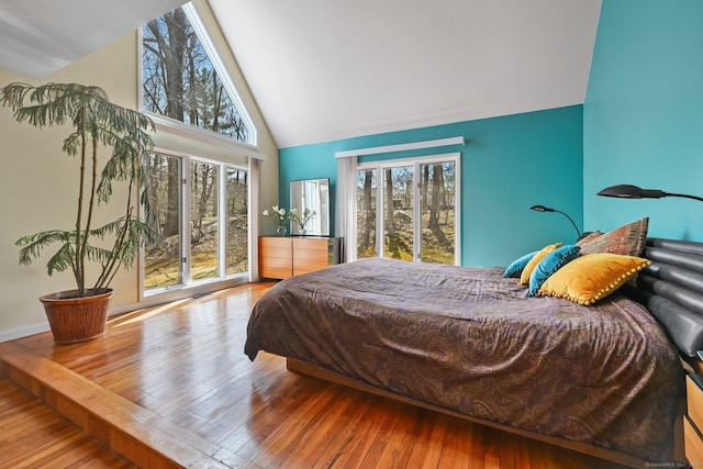 bedroom featuring high vaulted ceiling, multiple windows, wood finished floors, and access to exterior