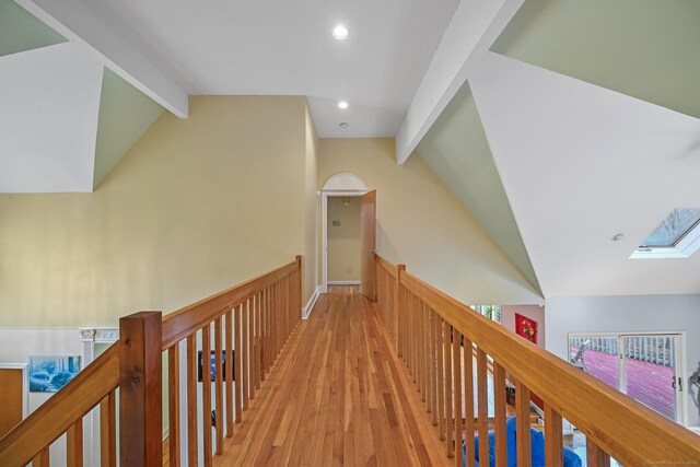 corridor featuring lofted ceiling with skylight, light wood-type flooring, recessed lighting, a wainscoted wall, and an upstairs landing