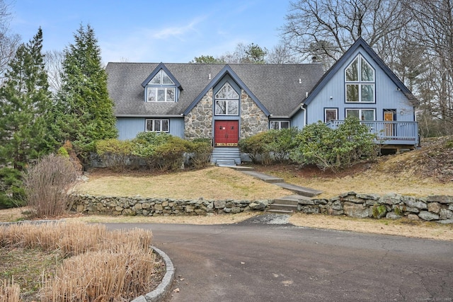 view of front of property featuring roof with shingles, a front yard, and stone siding