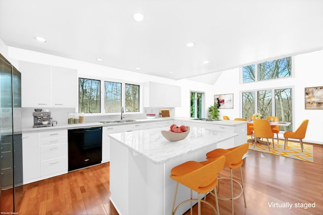 kitchen featuring a breakfast bar area, modern cabinets, a sink, black dishwasher, and light wood-style flooring