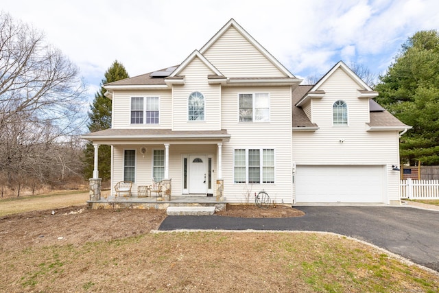view of front of home with driveway, roof with shingles, fence, solar panels, and a porch
