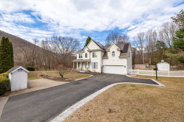 view of front of home with fence, a garage, a front yard, driveway, and a shed