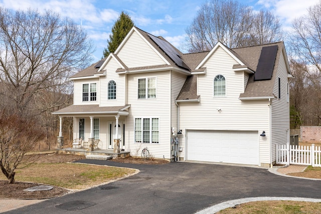 view of front of home with fence, solar panels, driveway, covered porch, and a shingled roof