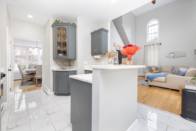 kitchen featuring light countertops, a peninsula, marble finish floor, glass insert cabinets, and gray cabinets
