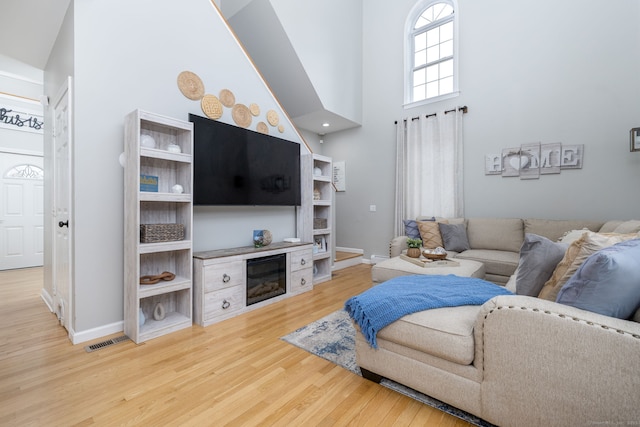 living room featuring baseboards, a high ceiling, visible vents, a glass covered fireplace, and wood finished floors