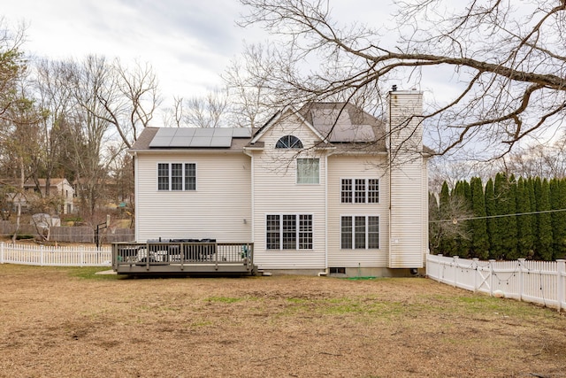 back of house with a wooden deck, a chimney, a fenced backyard, and a lawn