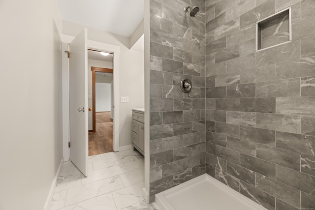 full bathroom with vanity, baseboards, marble finish floor, and tiled shower