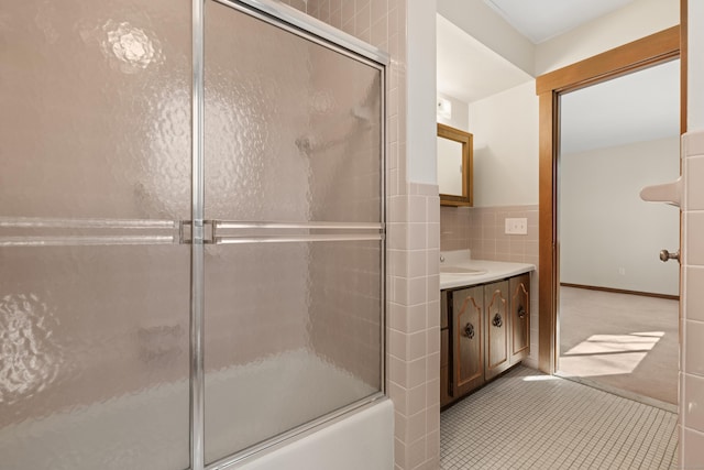 full bath with vanity, wainscoting, shower / bath combination with glass door, tile patterned floors, and tile walls