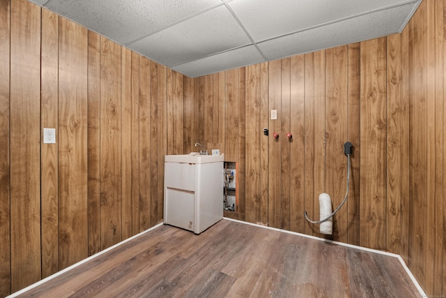 unfurnished room with a sink, wood walls, a paneled ceiling, and wood finished floors